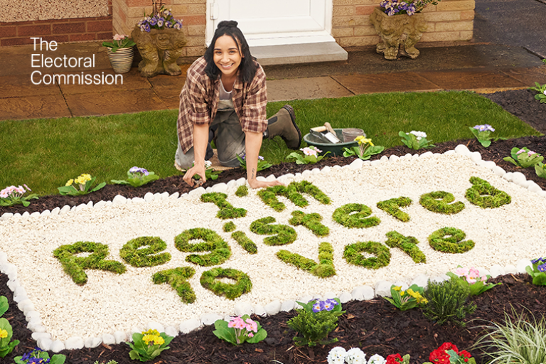 Woman crouched in garden next to foliage that spells out 'I'm registered to vote'