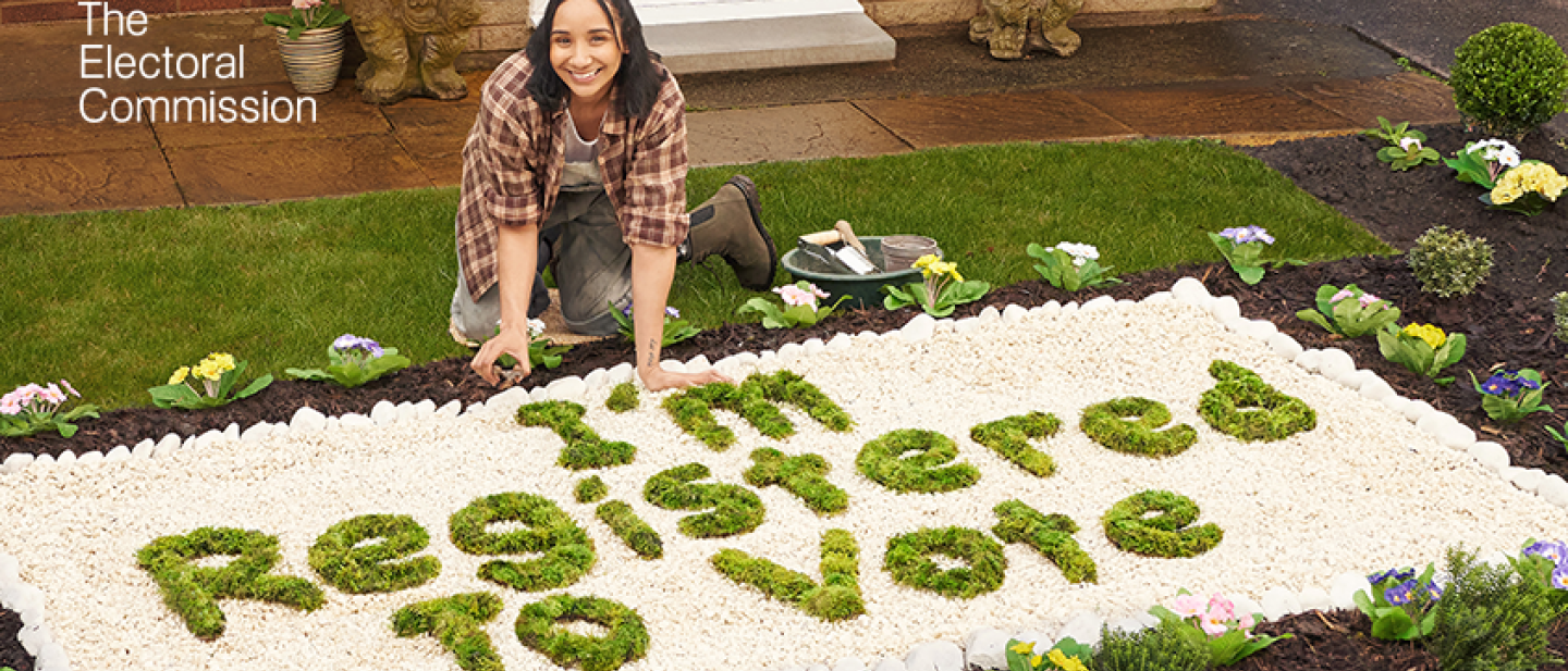Woman crouched in garden next to foliage that spells out 'I'm registered to vote'